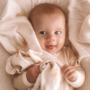 Smiling baby boy - playing with swaddle baby blanket in cot